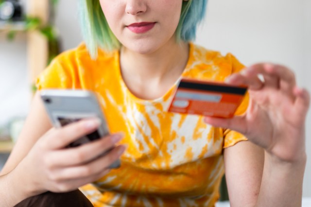 An image of a woman holding her phone in one hand and a credit card in the other