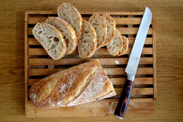 An image of a loaf of bread, slices, and a bread knife on a wooden cutting board