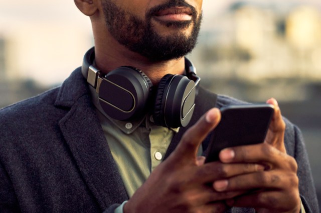 An image of man with headphones around his neck holding his phone