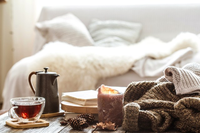An image of a living room with a cup of tea and a kettle, near a burning candle and a knitted sweater