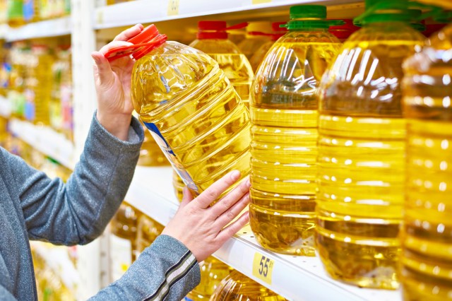 An image of a person pulling a large bottle of oil off a shelf