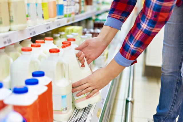 An image of a person taking a container of milk off a grocery store shelf