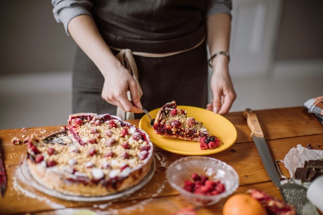 An image of a person putting a slice of berry pie on a yellow plate