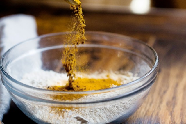 An image of a yellow spice being poured into a bowl of flour