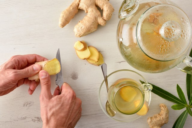 An image of a person cutting ginger root next to a kettle of ginger tea