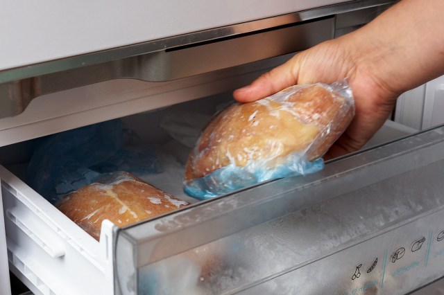 An image of a hand taking a loaf of bread out of the freezer