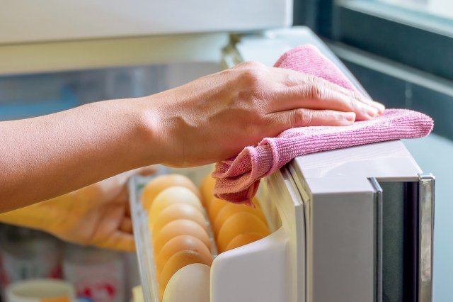 An image of a hand wiping down the top of the refrigerator door with a pink towel