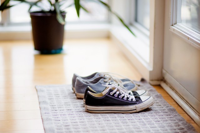 An image of two pairs of sneakers on a doormat by a door