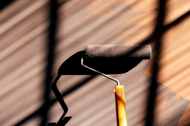 An image of a hand rolling brown paint onto a wall