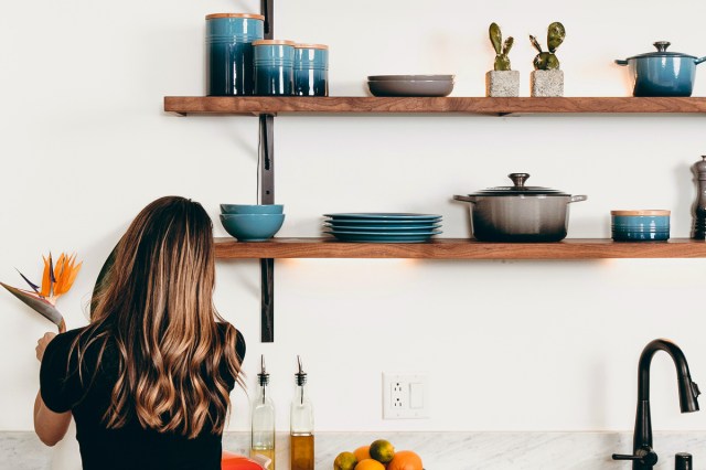 An image of a woman standing in a kitchen with shelves holding kitchenware