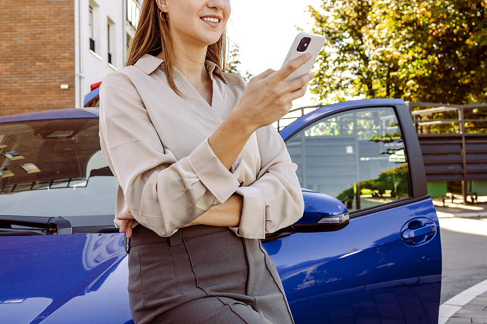 An image of a woman on her phone leaning against a car