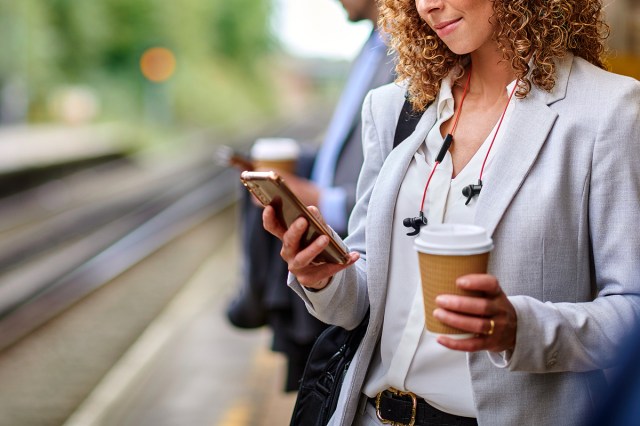 An image of a woman holding her phone phone in one hand and a cup of coffee in the other