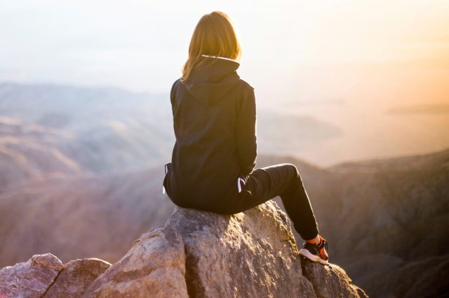 An image of a woman sitting on top of a mountain looking at the sunset