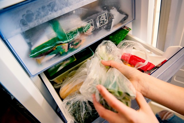 An image of a person taking vegetables out of a refrigerator drawer