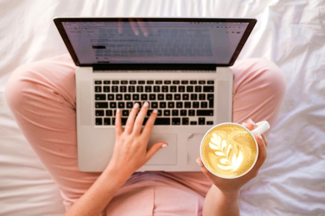 An image of a woman in bed with a laptop and a cup of coffee