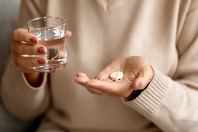 An image of a person holding a glass of water and a large pill