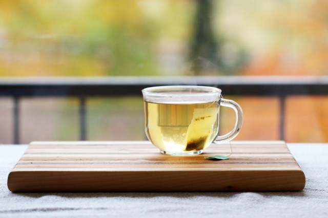 An image of a clear mug of green tea on a wooden cutting board