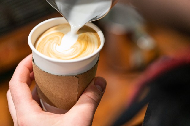 A close-up image of a barista pouring milk into a latte