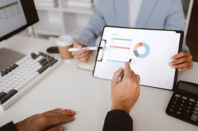 An image of a person pointing to a graph on a clipboard