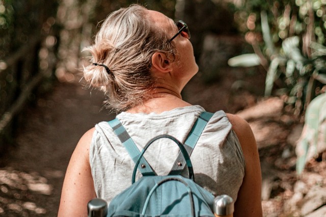 An image of the back of a woman wearing a backpack in the woods