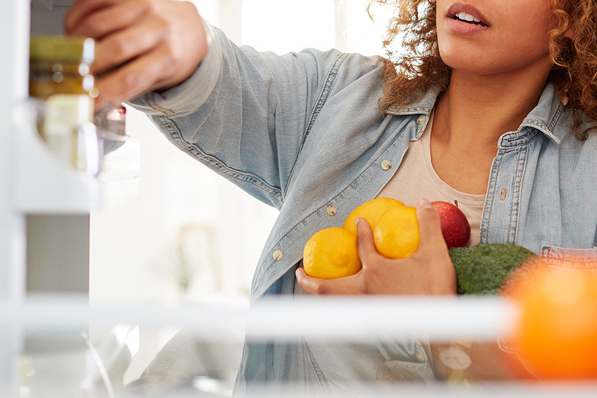 An image of a woman holding fruit in front of an open refrigerator
