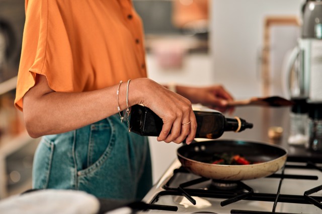 An image of a woman pouring oil into a pan on the stove
