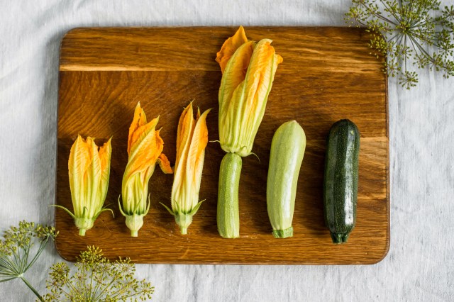 An image of squash and squash blossoms on a wooden cutting board