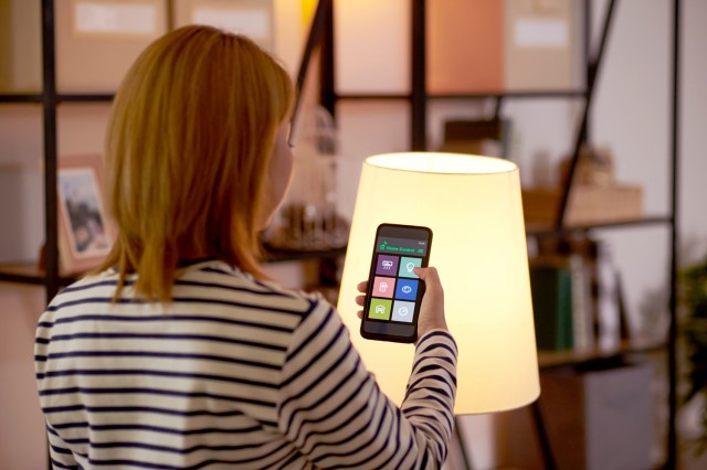 An image of a woman using an app on her phone to turn off a light
