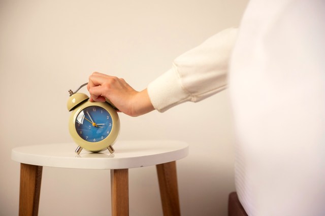 An image of a person in bed hitting an alarm clock on a nightstand
