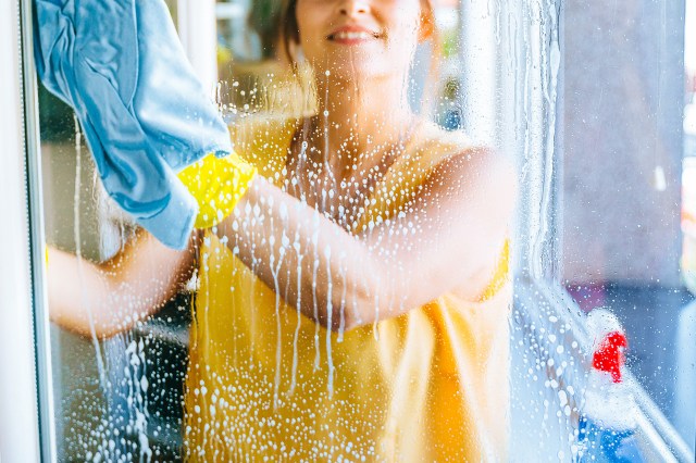 An image of a woman cleaning a window with glass cleaner