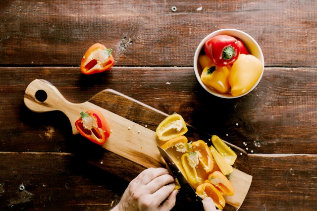 An image of a person chopping bell peppers on a wooden cutting board