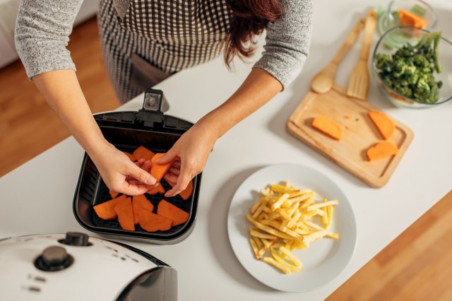 An image of a woman putting sweet potatoes into an airfrie