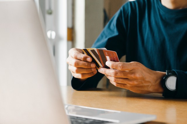 An image of a man holding three credit cards in front of a laptop