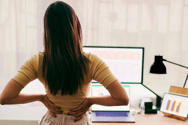 An image of a woman holding her back in front of a work dest setup