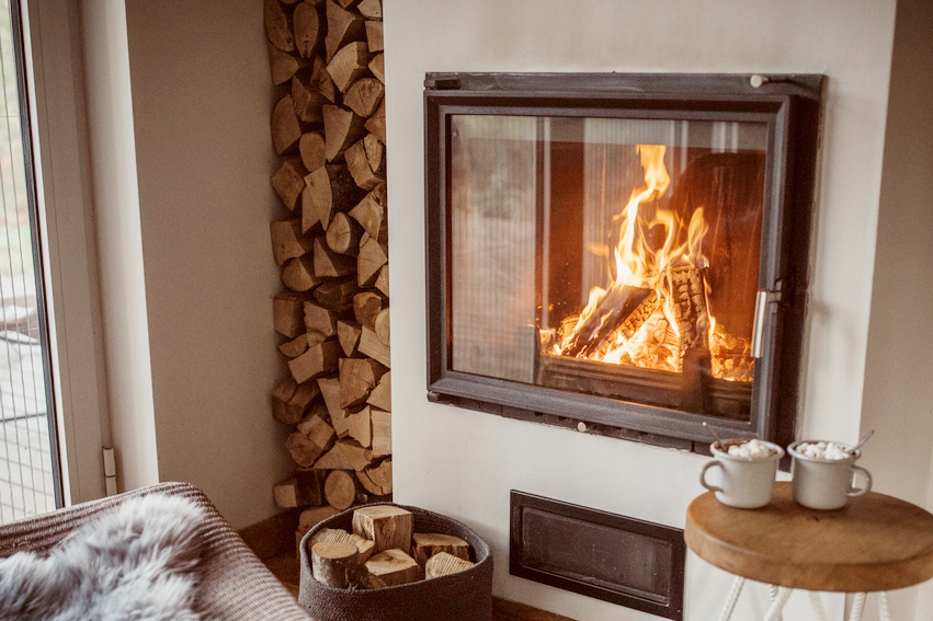 An image of a cozy fireplace with firewood stacked to the left