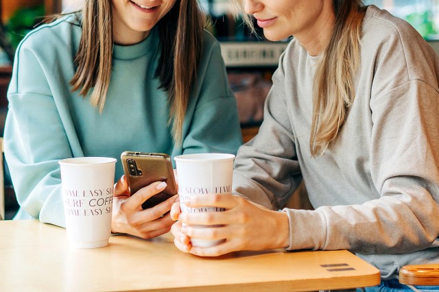 An image of two women looking at a phone at a coffee shop