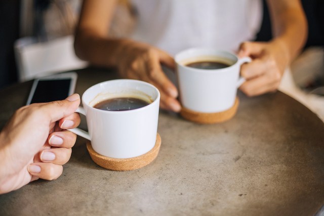 An image of two people holding white mugs of coffee