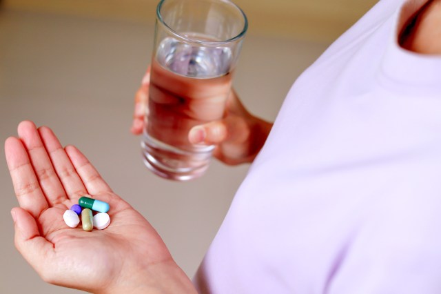 An image of a woman holding pills in one hand and a glass of water in the other