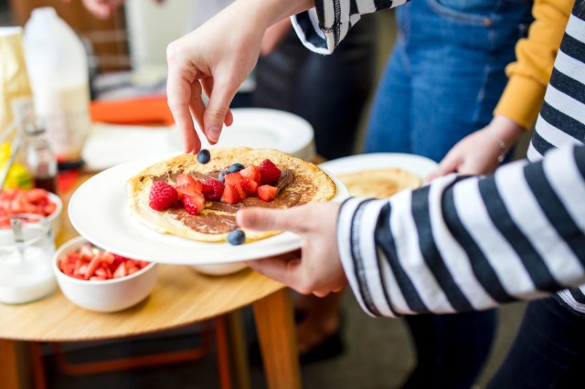 An image of a person holding a plate of pancakes with fruit