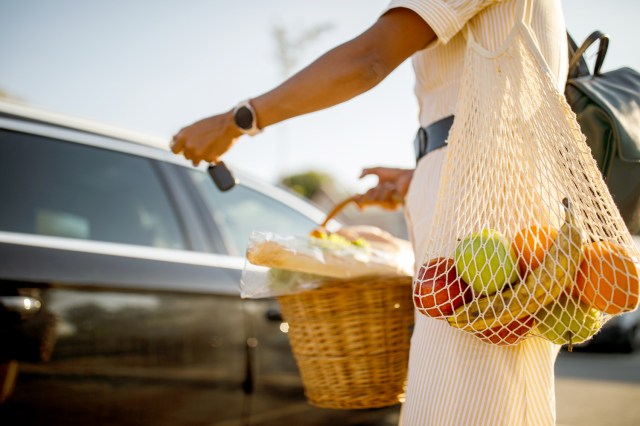 An image of a woman in a parking lot with a mesh bag of fruit over her shoulder