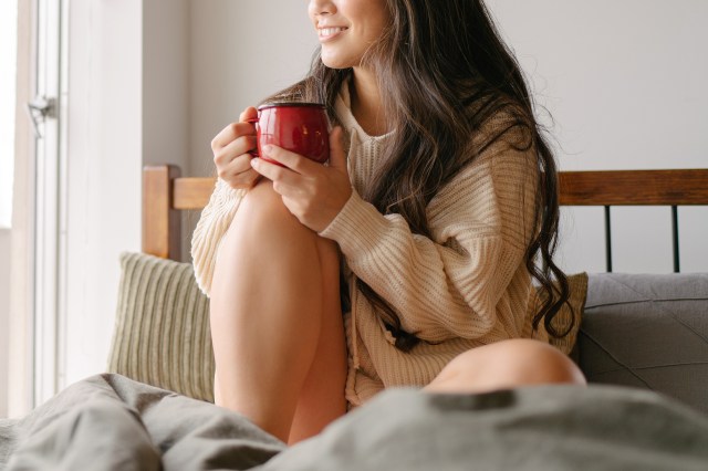 An image of a woman holding a mug while sitting on a bed