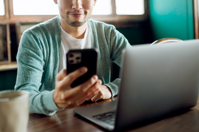 An image of a man holding a phone in front of a laptop