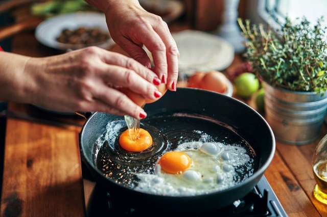 A pair of hands crack two eggs into a cast-iron pan