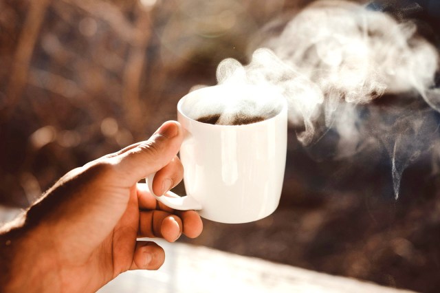 An image of a person holding a steaming mug of coffee