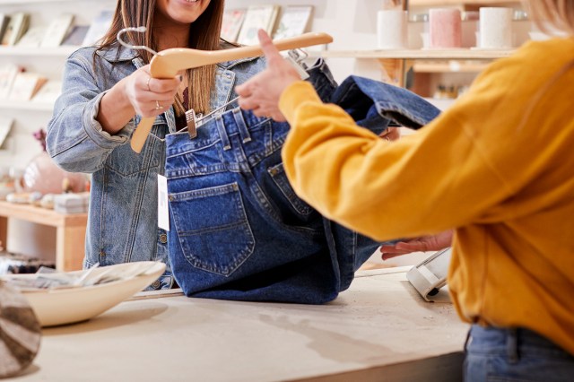 An image of a woman handing a pair of jeans over to a register clerk