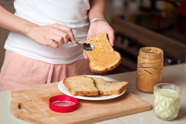 An image of woman spreading peanut butter on bread