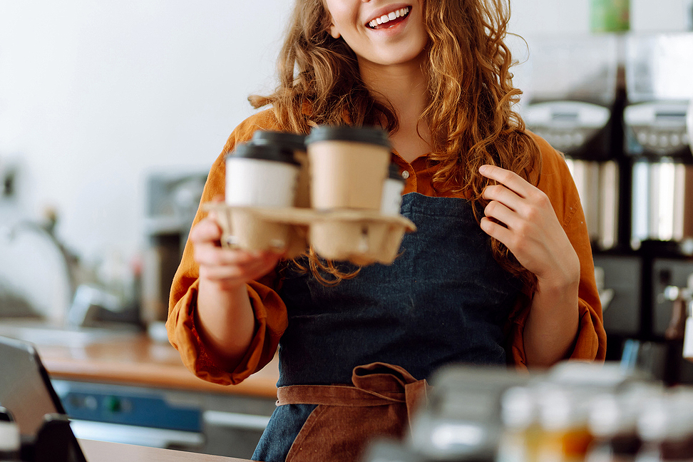 An image of a female barista holding to-go cups of coffee