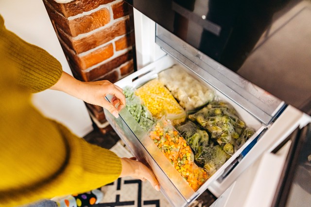 An image of a woman opening a freezer filled with vegetables
