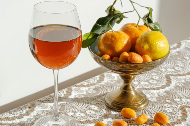 An image of a glass of wine next to a bowl of citrus fruit