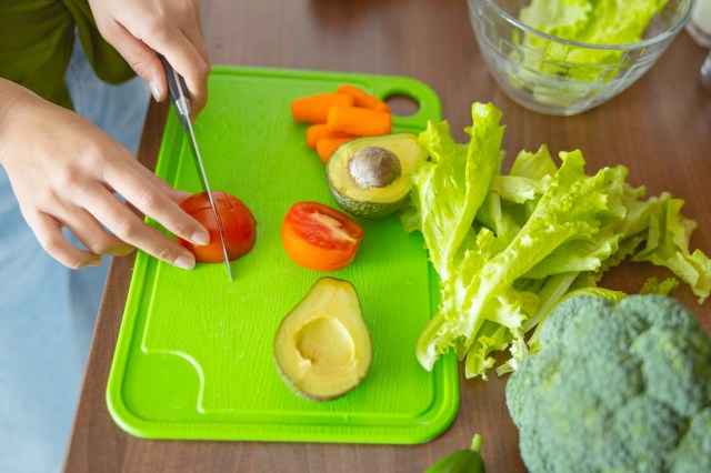 An image of a person cutting vegetables on a green cutting board